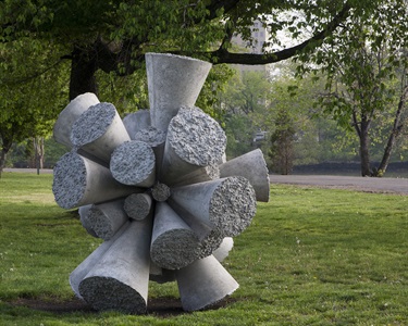 A grey abstract sculpture in a park. 