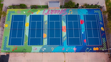 A colorful design painted on the ground around a tennis court. 