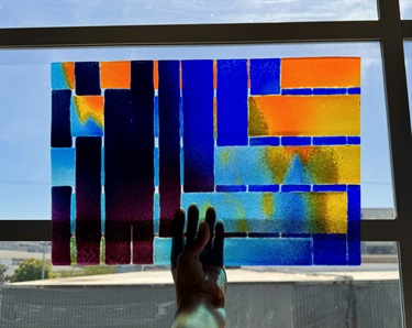 A hand holding up a colorful piece of glass to the light. 