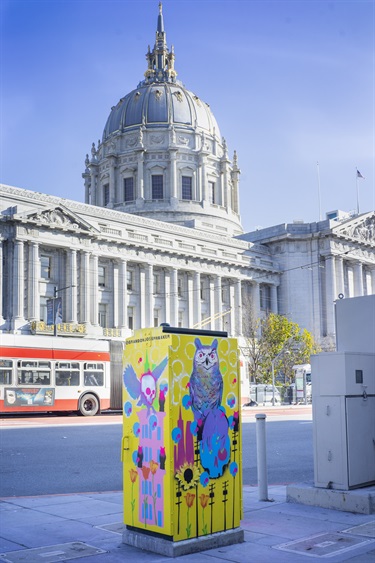A painted utility box in front of a city building. 