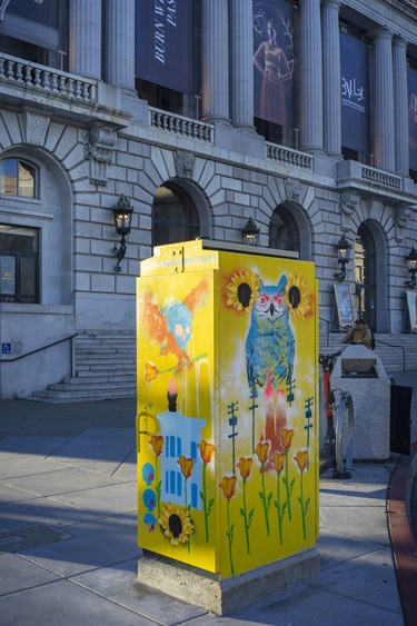 A painted utility box outside a city building. 