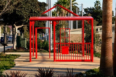 A red metal sculptural structure in a park. 