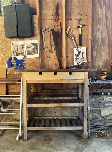A wood working table with tools hanging on the wall. 