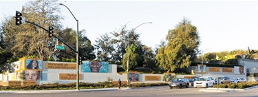 A series of murals on the side of a wall along a road. 