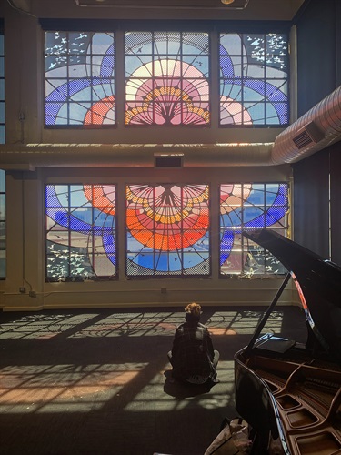 A person sitting in a room in front of a colored glass window.