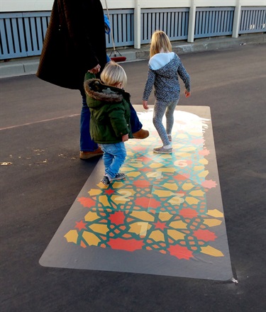 Two children playing on a piece of artwork on the ground.