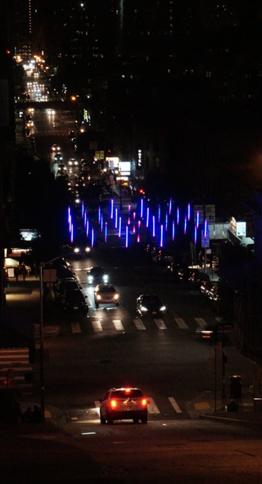 An illuminated abstract sculpture above a street.