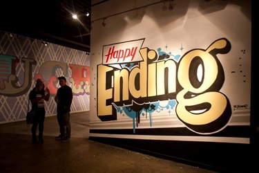 Two people standing next to a mural with text on a wall. 