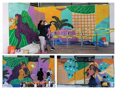 People taking a picture in front of a mural on the side of a building. 