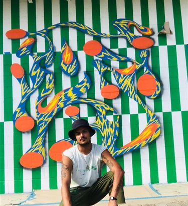A person kneeling in front of a mural painted on a wall. 