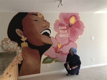 A person kneeling next to a mural painted on a wall. 