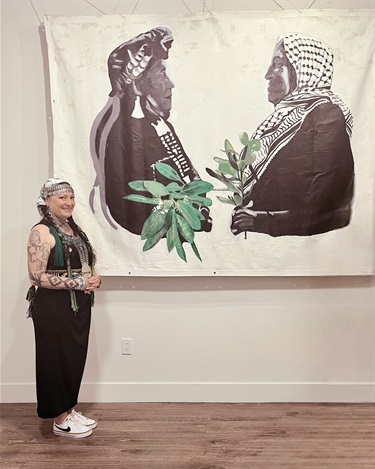 A person standing next to a piece of artwork hung on a white wall. 