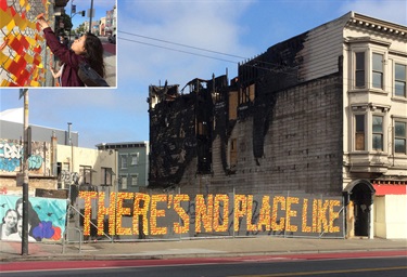 AN art installation made of plastic on chain-link fence next to a fire damaged lot. 