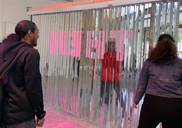 People viewing an art installation made of Mirrored mylar, vertical blinds, “I voted” stickers.