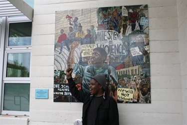 A person standing in front of a  piece of artwork installed on a building wall.