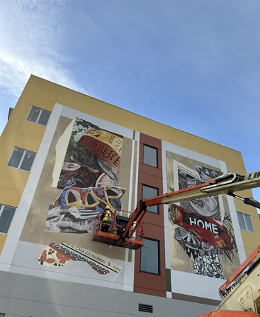 A person in a lift painting a mural on the side of a building. 