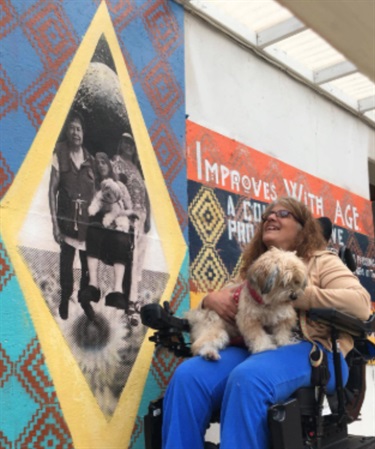 A person holding a dog and looking at artwork on a wall. 
