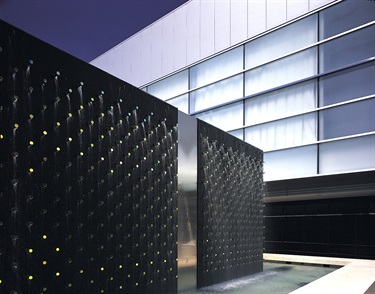 An abstract sculpture in a fountain in front of a building.