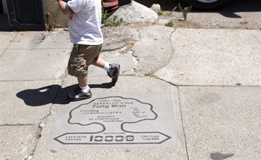 Feet walking past a tree-shaped marker in the concrete of the sidewalk.
