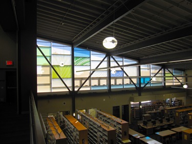 Blue and green designs on rectangular window panes inside a library. 
