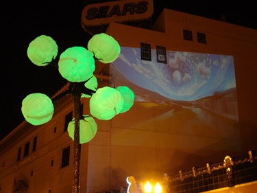 A green light sculpture in front of an image being projected on a wall. 