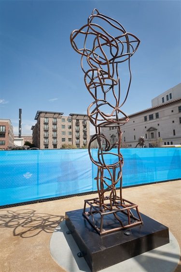 A metal sculpture in front of apartment buildings. 