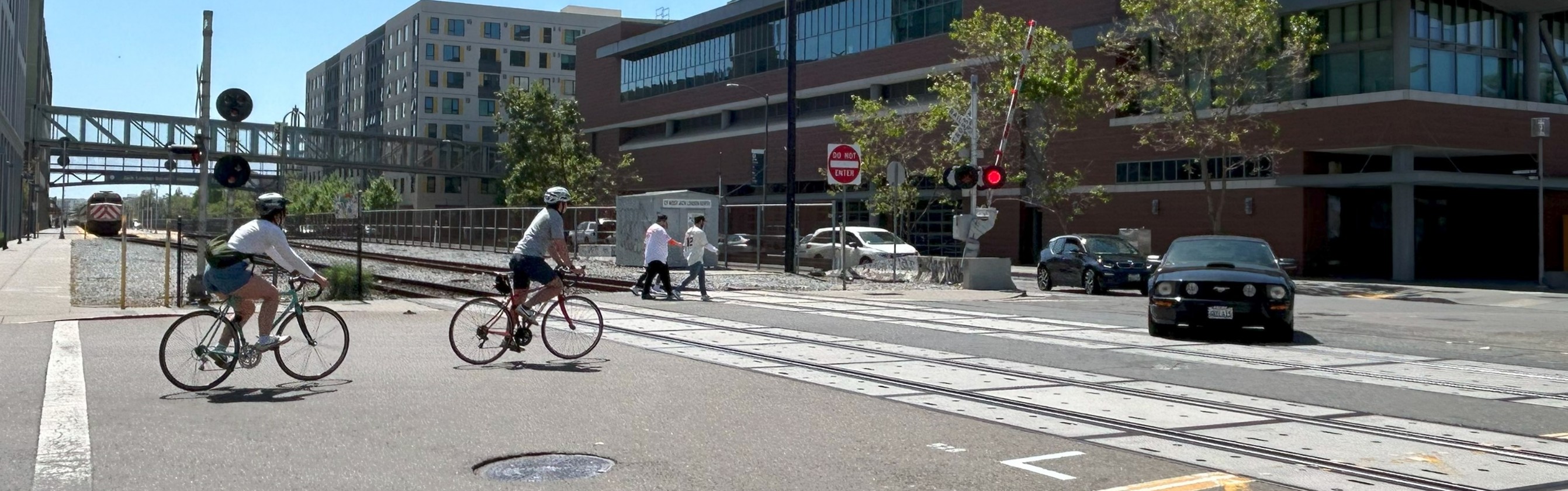 A photo showing pedestrians, bicyclists, and drivers crossing railroad tracks on Embarcadero West at Webster Street