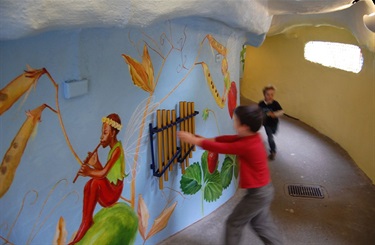A child interacts with chimes on a wall surrounded by a painted mural at Fairyland.
