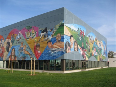 A colorful mural of people in various recreational activities on the exterior of a sports center. 