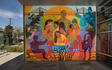 A colorful mural showing people in various activities. The mural in on the exterior wall of a recreation center entryway.