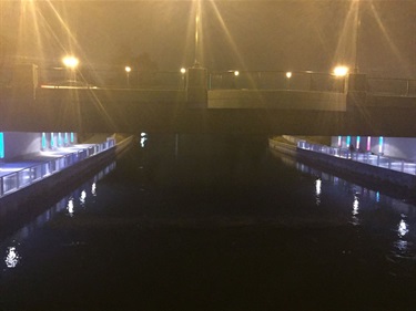 A colorful light installation under a bridge along a water canal. 