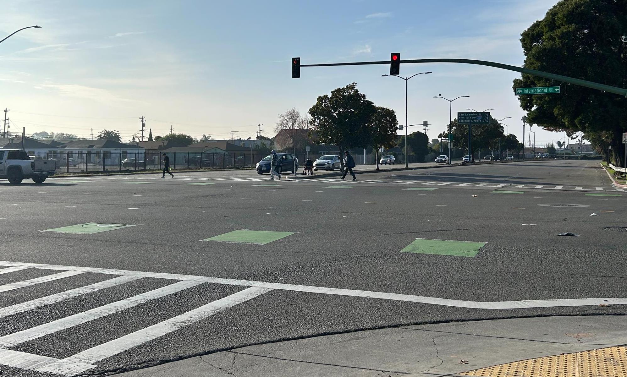 Photo of Hegenberger Road at International Boulevard. Image shows three pedestrians crossing Hegenberger.