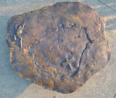 Bronze relief mold with designs set into the concrete of a sidewalk. 